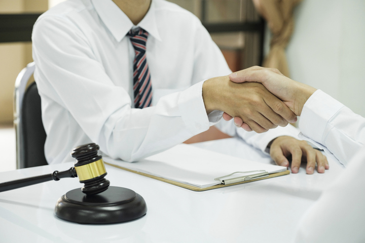Business handshake with gavel and documents on table.
