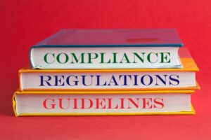 Stacked books labeled compliance, regulations, guidelines.