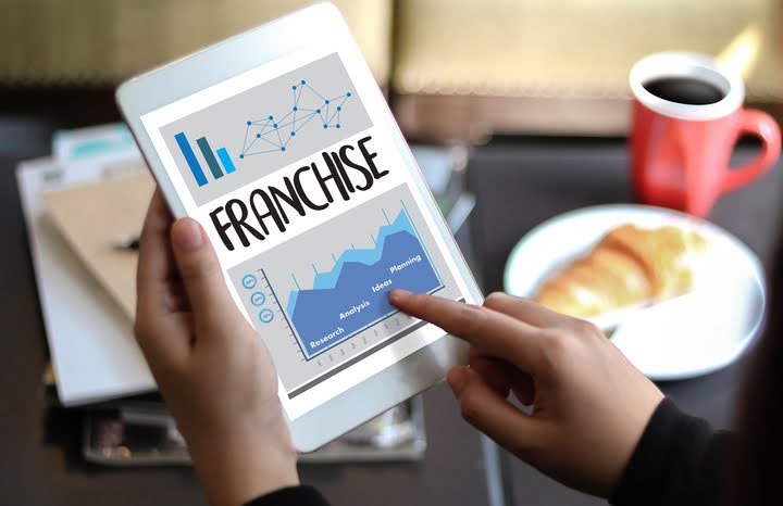Person reading franchise data on tablet with coffee.