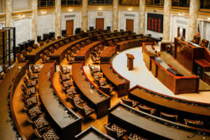 Empty legislative chamber with rows of seats and podium.