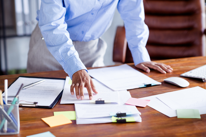 Person organizing documents on cluttered office desk.