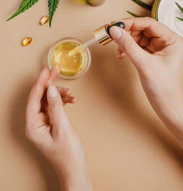 Hands holding cannabis oil dropper over skincare products